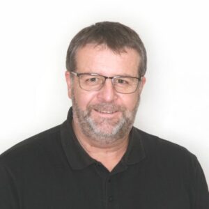 Paul Retter, homme barbu avec des lunettes et un polo noir, souriant devant un fond blanc