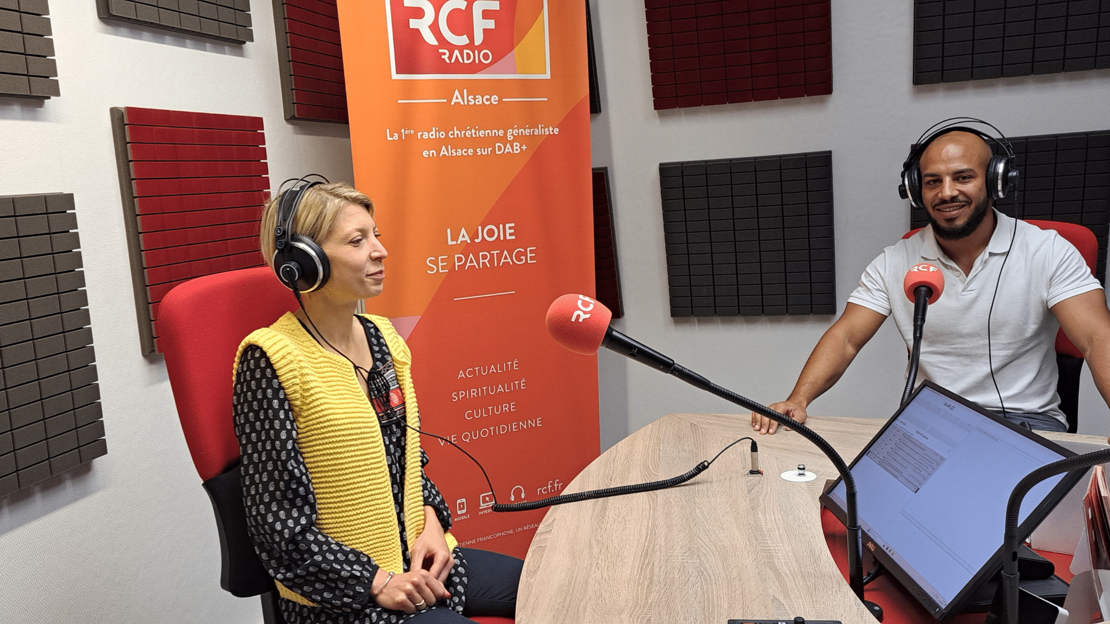 Johanna Rivière et Cyprien Peronet en studio, enregistrant l'émission Polychrome sur RCF Alsace, avec des micros et un fond aux couleurs de la radio