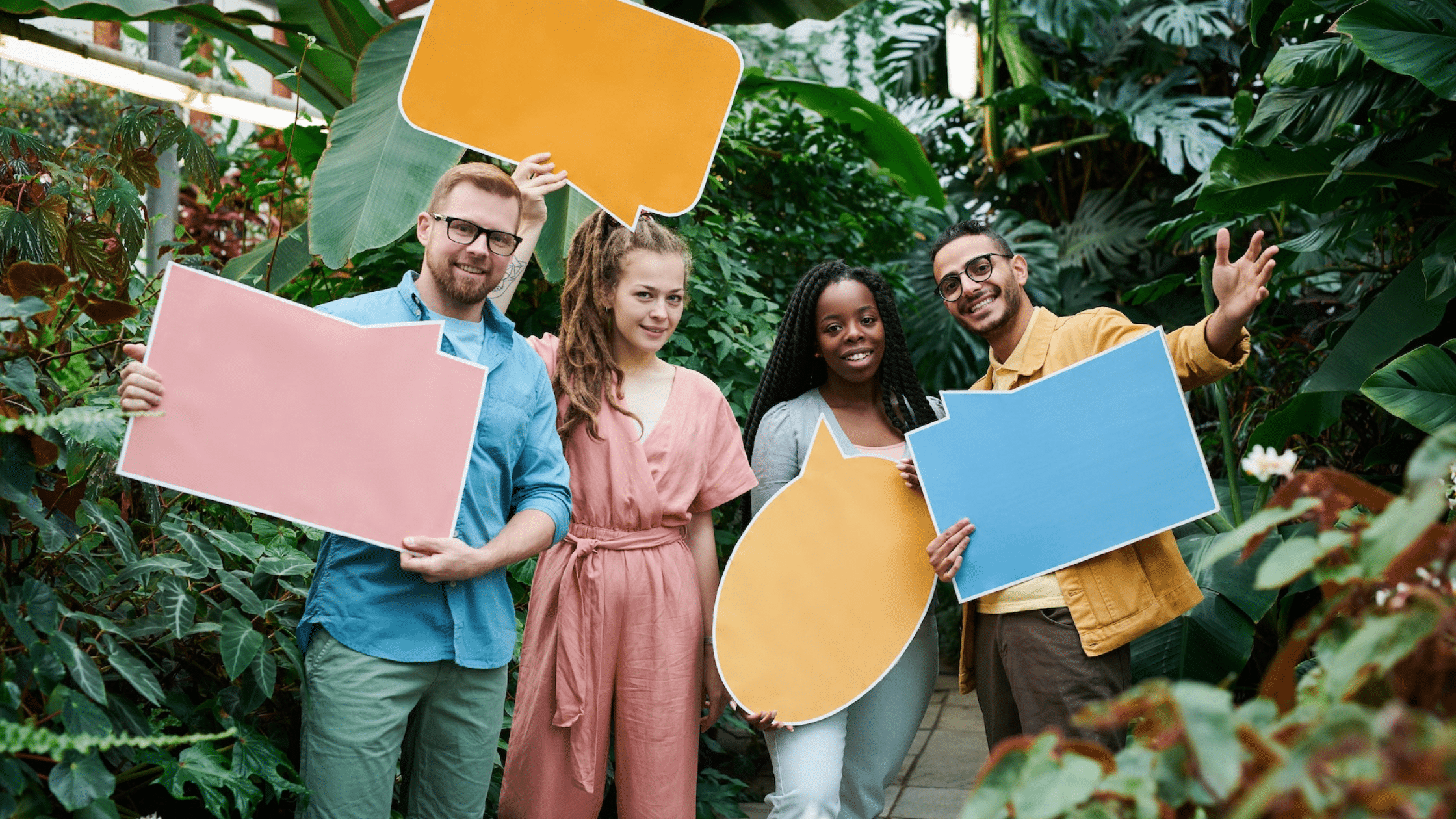 Quatre personnes souriantes tenant des bulles de dialogue colorées dans un environnement verdoyant, symbolisant la communication et l'échange d'idées